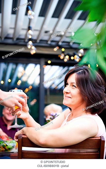 Mature woman getting handed wine at family lunch on patio table