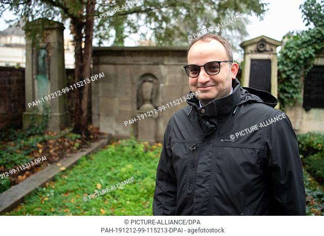 12 December 2019, Baden-Wuerttemberg, Mannheim: Martin Geipel, teacher at the Johanna-Geissmar-Gymnasium, stands in front of a tomb in Mannheim's main cemetery