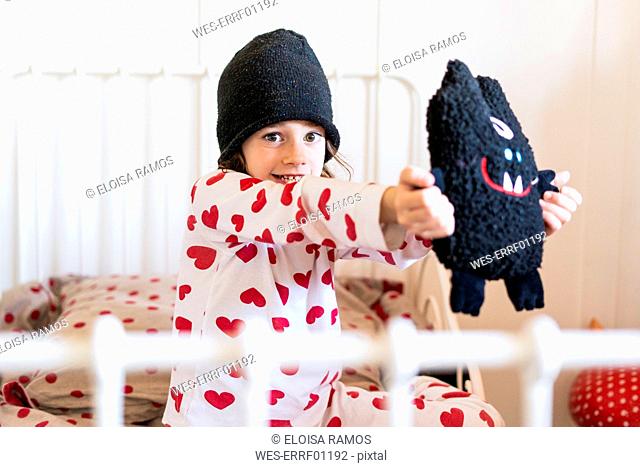 Portrait of little girl wearing cap sitting in bed with her soft toy