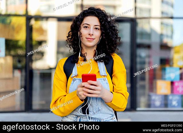 Young woman holding mobile phone listening to music through in-ear headphones