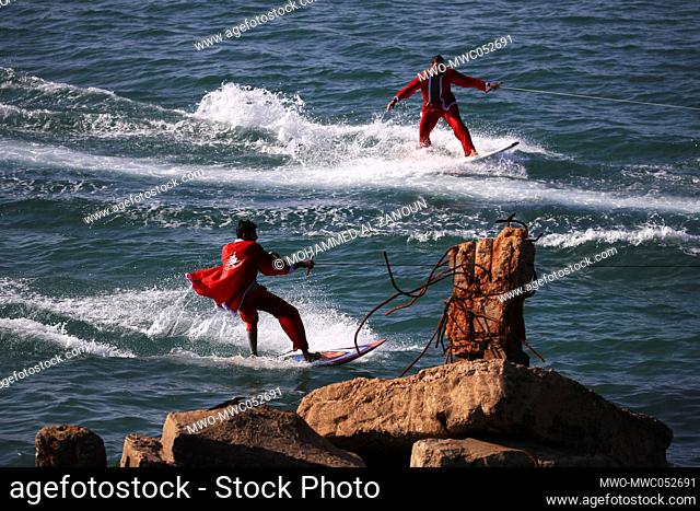 Palestinian surfers dressed in Santa Claus outfits surfing in Mediterranean waters. Gaza City. Palestine