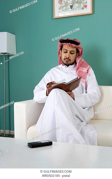 Arab man sitting on sofa, writing