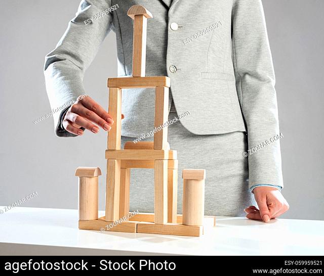 Business woman building construction on table from wooden blocks. Strategy planning and company development. Young woman wearing formal wear sitting in office...