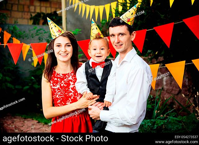 theme children birthday party. Family father and mother holding son of one year on the background of greenery and festive decor, garlands and colored ornaments