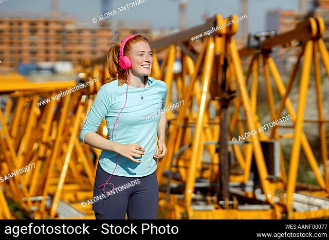 Young woman with headphones running at construction site