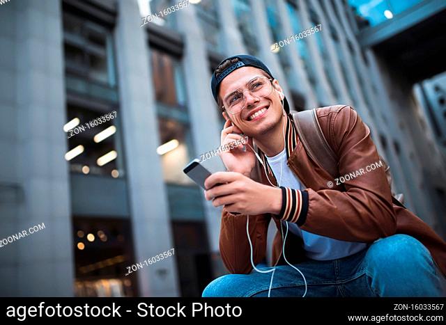 Man Sitting Listening Music Earphones Concept. Cheerful young guy listening the music