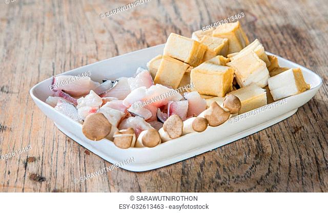 Meat, fish, mushroom and tofu dish in white placed on a wooden table. Focus on fish