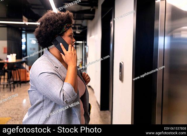 Mid adult biracial businesswoman talking on smartphone while waiting for elevator at office