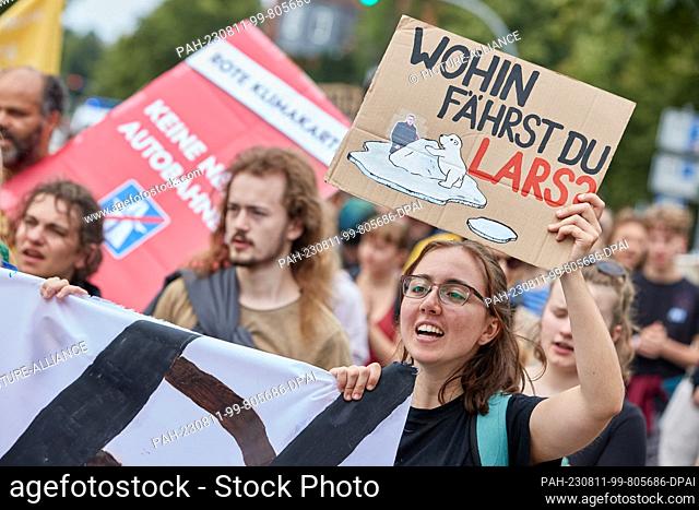 11 August 2023, Lower Saxony, Lüneburg: A participant in a protest march of the climate movement Fridays for Future carries a cardboard sign with a drawing of a...
