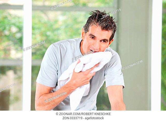 Schwitzender Mann im Fitnesscenter trocknet sich mit Handtuch ab