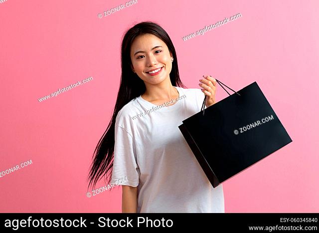 Shopping asian happy woman holding shopping bags on pink background and smiles