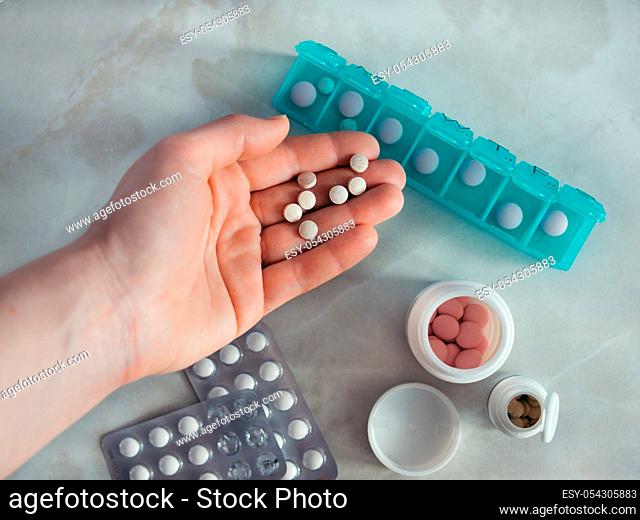 Hand with pills and pillbox. Top view of seven day pill box with pills. Green pill-box over light marble table. Open pill box and open boxes with pills or...