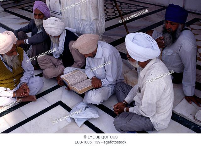 Group of Sikh men reading from holy book on black and white marble floor of the Golden Temple complex
