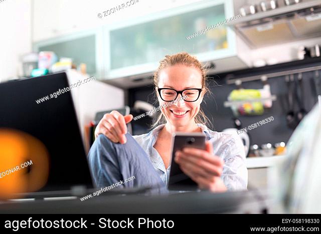 Stay at home and social distancing. Woman in her casual home clothing working remotly from kitchen dining table. Video chatting using social media with friend