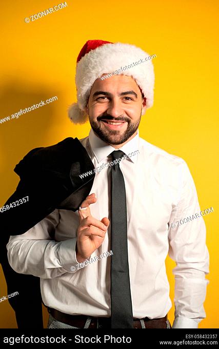 Bearded smiling handsome business man in Santa hat wearing grey suite posing holding his jacket on his shoulder, hanging it behind looking lowering sunglasses...