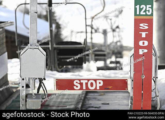 23 February 2021, France, Notre-Dame-De-Bellecombe: A barrier with the inscription ""Stop"" stands in front of an empty chairlift hanging over the road