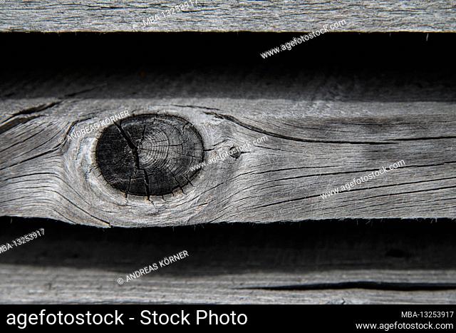 Faded, parallel wooden slats with knotholes in front of a black background