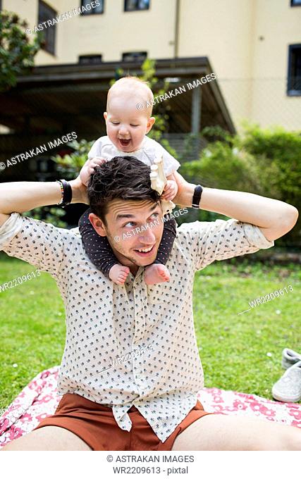 Playful baby girl sitting on father's shoulders at yard