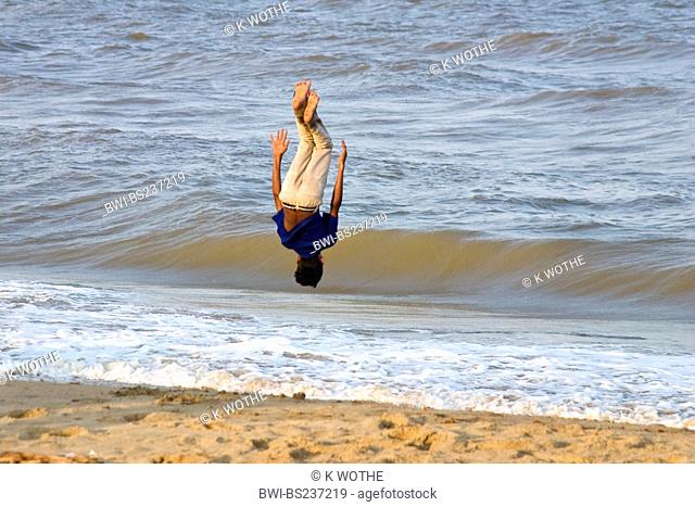 boy at sand beach doing a somersault in front of the waves, India, Tamil Nadu, Marina Beach, Chennai