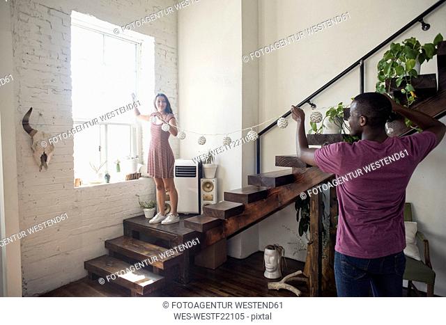 Young couple decorating loft with fairylights