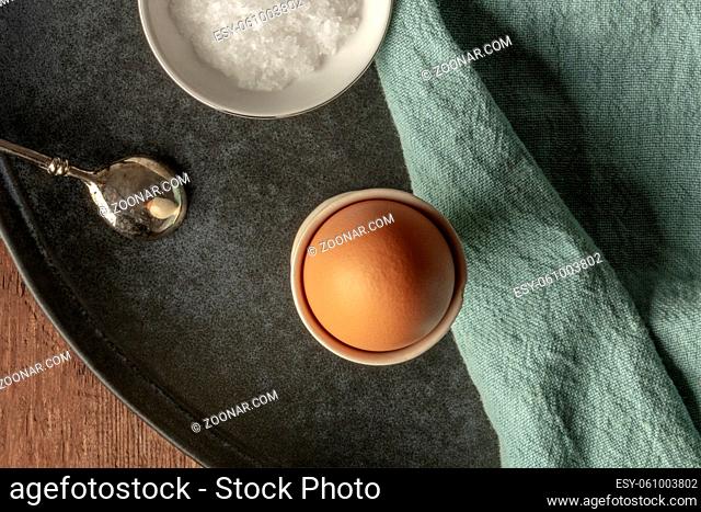 A boiled egg in an eggcup with coarse sea salt and a spoon, shot from above with copy space