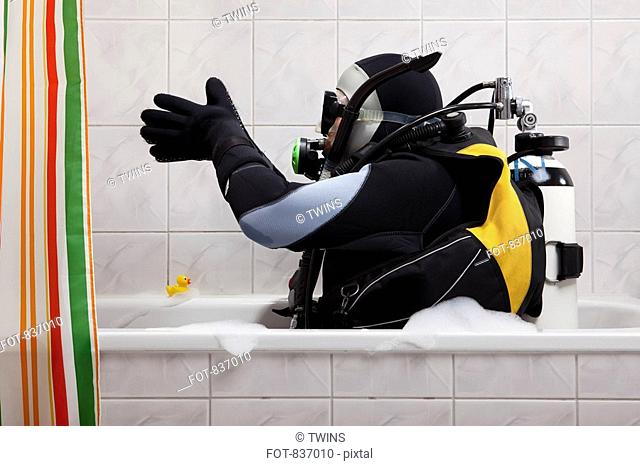 A scuba diver sitting in a bathtub preparing to dive in