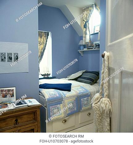 Blue patchwork quilt on built-in bed with storage drawers in small blue guest room