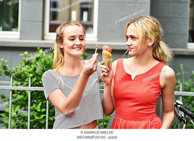 Two young women sharing an ice cream cone in the city