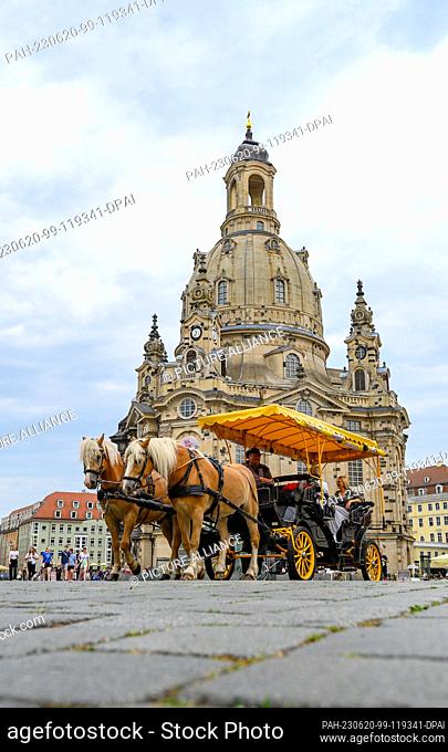 20 June 2023, Saxony, Dresden: A horse-drawn carriage drives along the Neumarkt in the old town in front of the Frauenkirche at noon with tourists