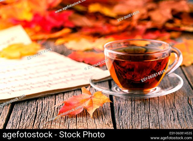 Relax time in fall season. Red maple leaf on table with tea