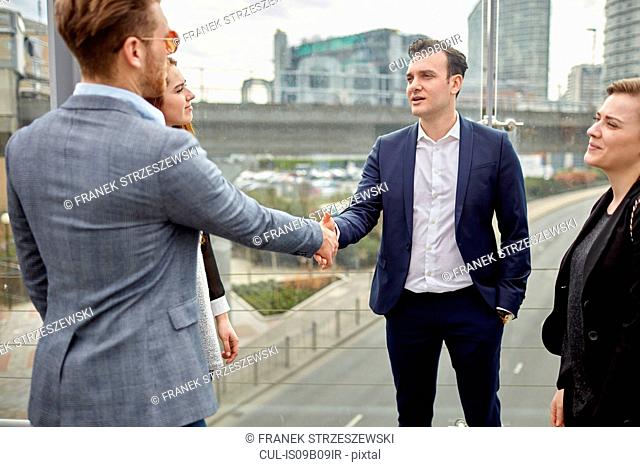 Businessmen and women shaking hands on city footbridge, London, UK