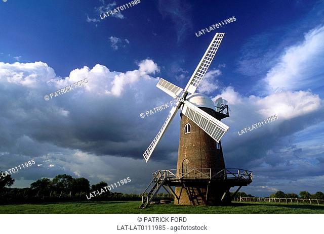 Working windmill. For corn grinding and milling. Stone tower. Wooden sails. Stormy clouds in sky