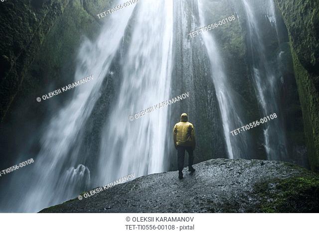 Man wearing yellow raincoat by Seljalandsfoss waterfall in Iceland