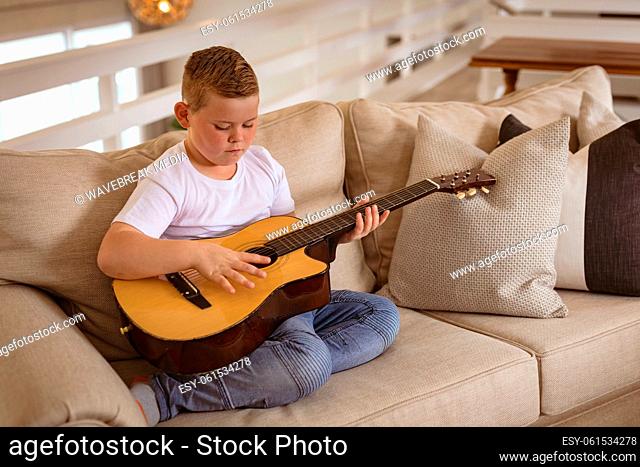 Caucasian boy playing guitar sitting on the couch in the living room at home