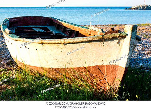 Old boat on the seashore covered with grass with calm sea in the background