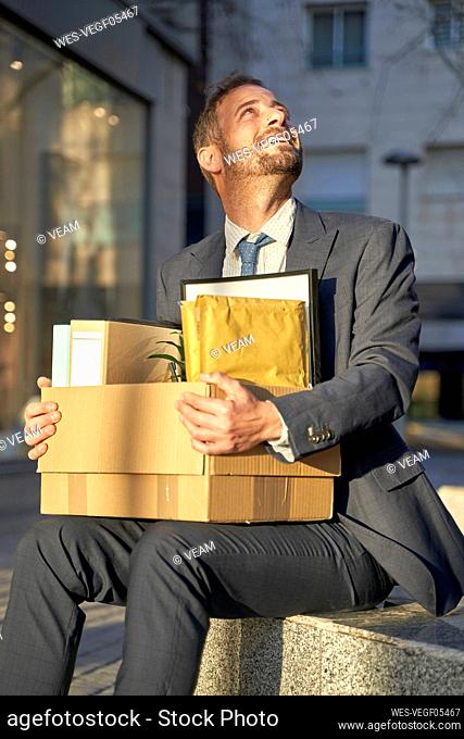 Smiling businessman with box sitting on bench