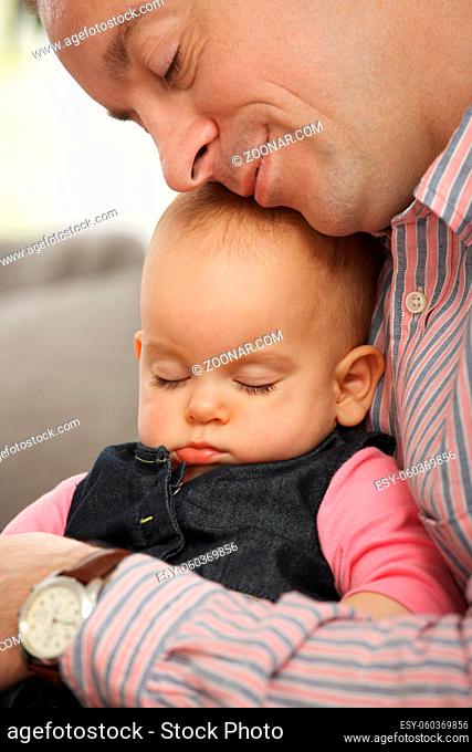 Cute little baby sleeping held in father's arm at home