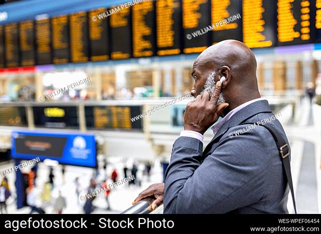 Businessman touching wireless in-ear headphones at railroad station