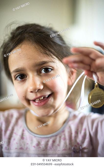portrait of a 6 year old girl showing a medal hanging from the neck in her home