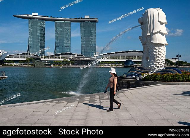Singapore, Republic of Singapore, Asia - A woman wearing a protective face mask amid the lasting corona crisis walks by the famous water fountain statue at...
