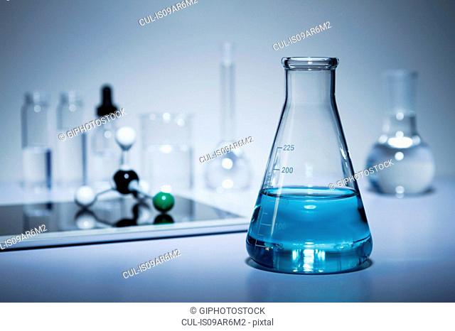 Chemistry research. Erlenmeyer flask containing colored liquid and a digital tablet with a ball-and-stick molecular model on its screen