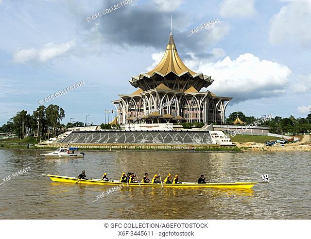 Longboat passing by the Sarawak State Legislative Assembly Building, Dewan Undangan Negri State Assembly, at Sarawak river, Kuching, Sarawak, Borneo, Malaysia