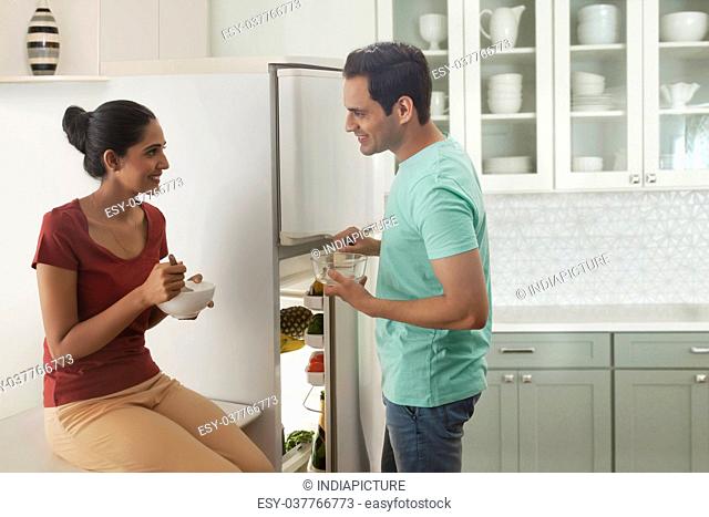 Couple eating in front of a refrigerator in the kitchen