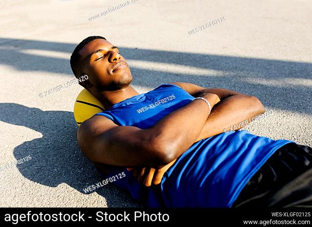 Young man resting head on basketball while lying down at sports court
