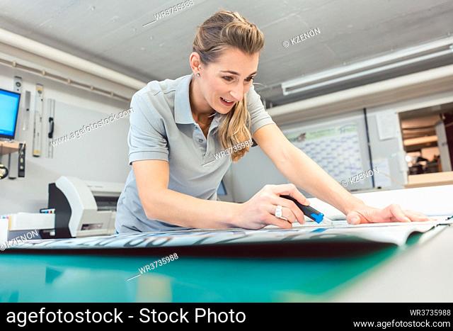 Woman cutting signs or vinyl wraps producing advertising materials in workshop of agency