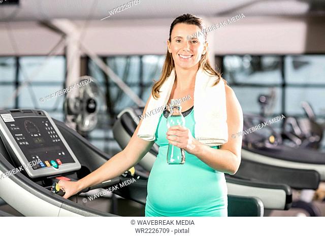 Smiling pregnant woman holding exercise mat and water bottle