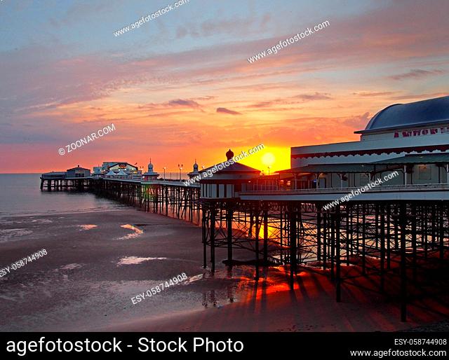 the sun setting over the historic north pier in blackpool with glowing light reflected on the beach and colourful twilight sky