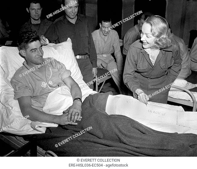 Marlene Dietrich, autographs the cast on the leg of 'Tec 4' Earl McFarland of Cavider, Texas. At a U.S. hospital in Belgium, Nov. 24, 1944