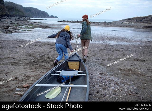 Young couple pulling canoe on beach, Kent, UK