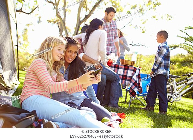 Two Girls Using Mobile Phone On Family Camping Holiday